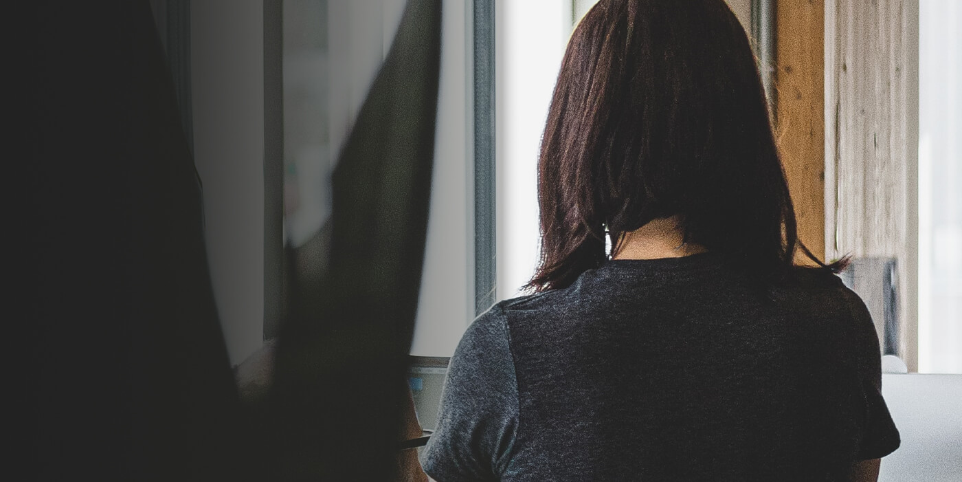 Woman with shoulder length hair in a dark gray shirt looking out a window